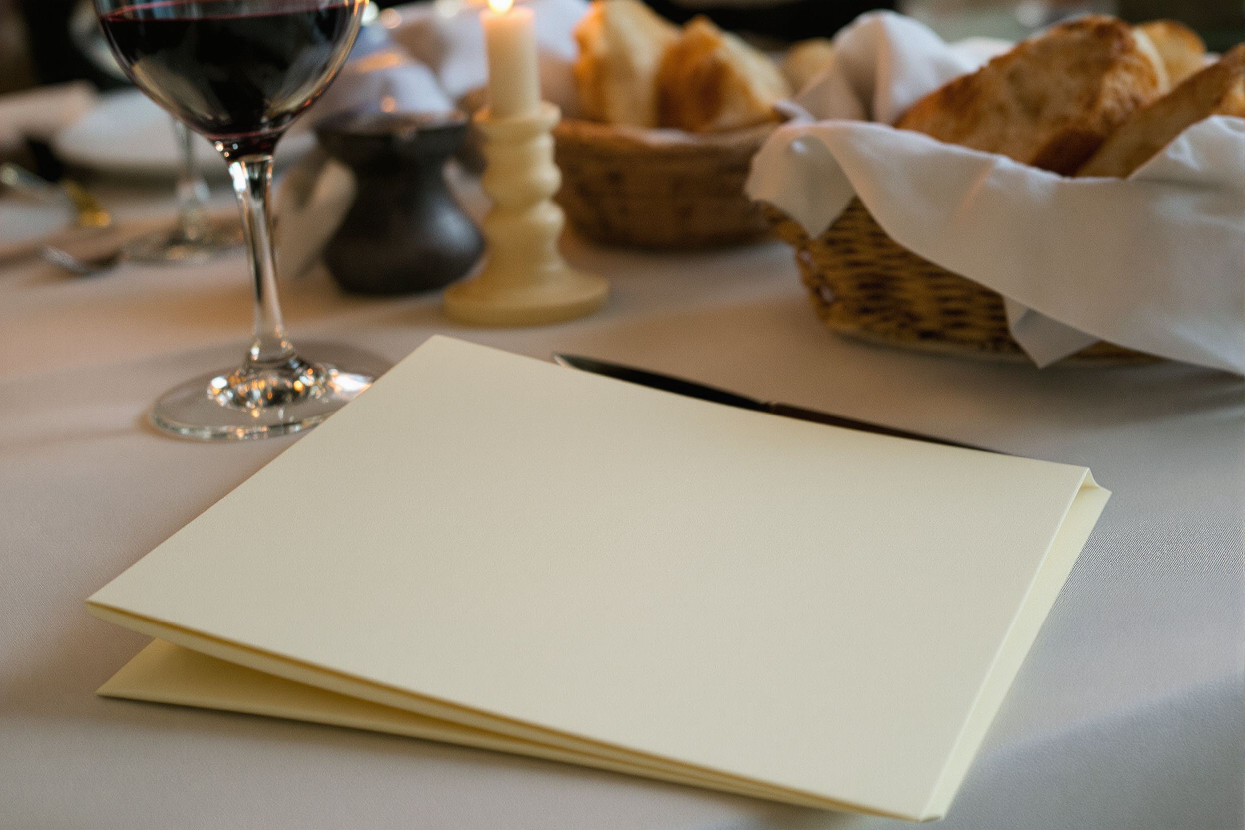 A closed menu card beside a wine glass and bread basket