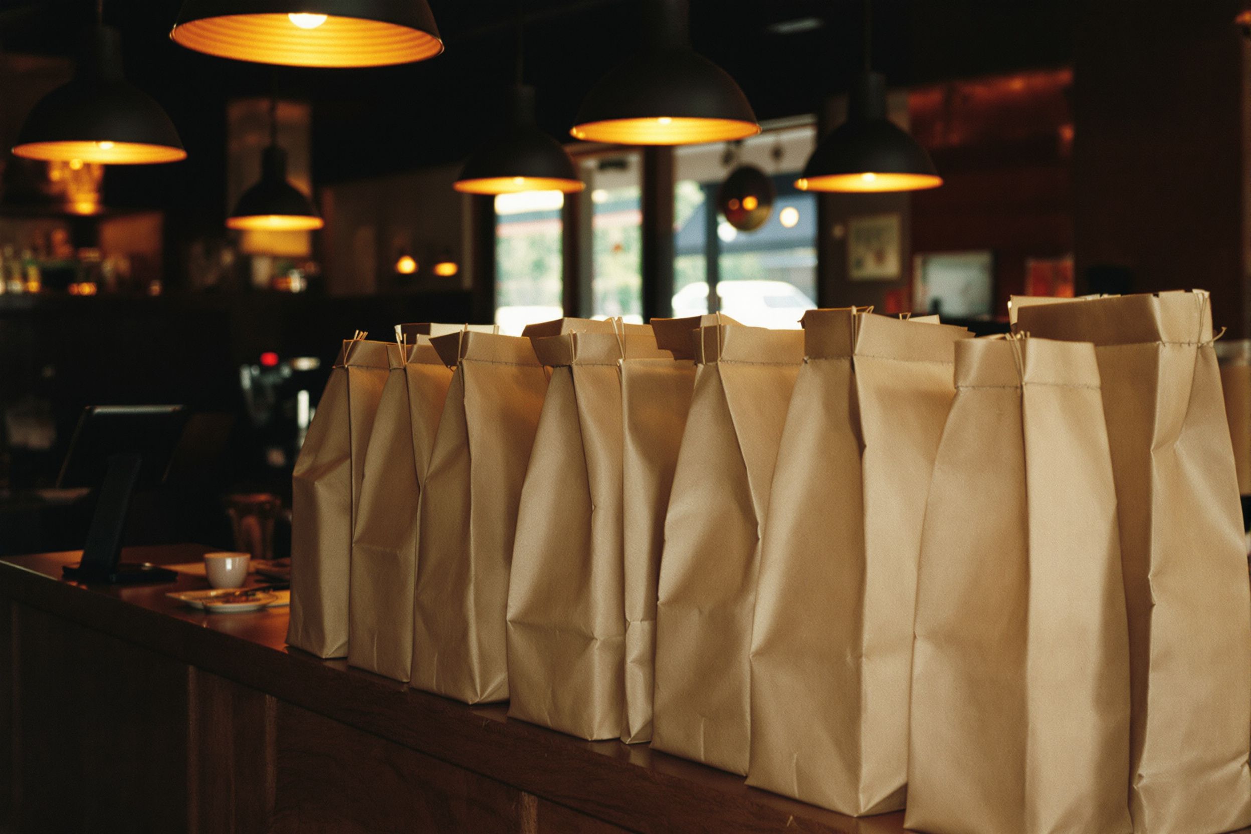 Stapled paper takeout bags lined up on a wooden pickup counter